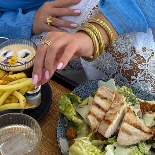 image of stack of gold bangles on ladies arm with food in background