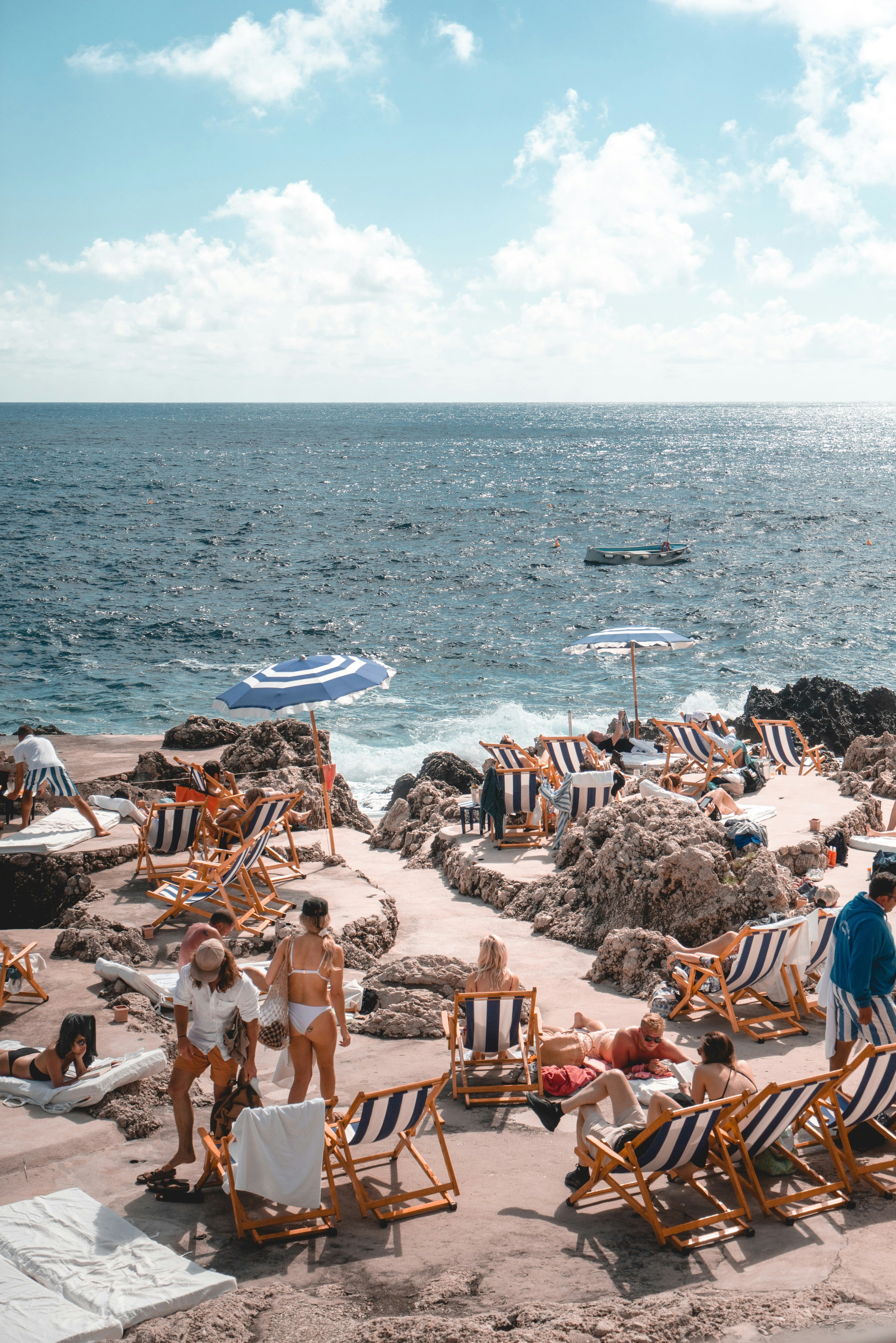 Image of an Italian beach cove with people in swimwear, and deckchairs on the shore

